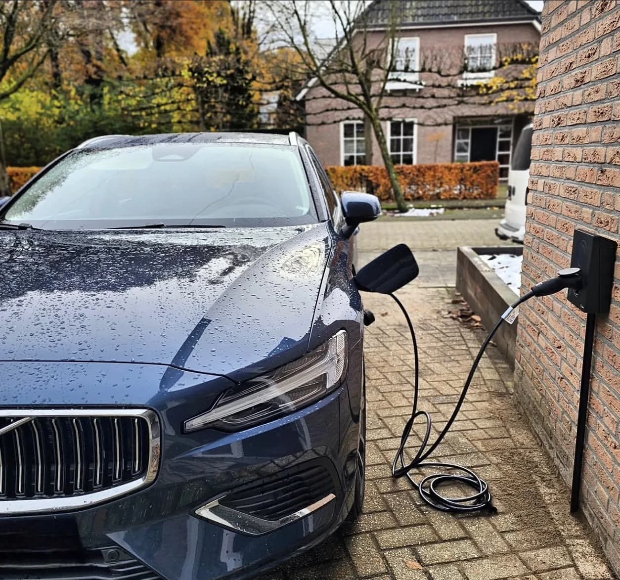 Laadpaal aan de gevel van een woning met een auto aan de laadkabel